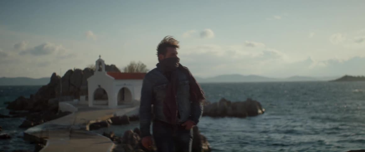 A man wearing a scarf walks along a rocky coastline