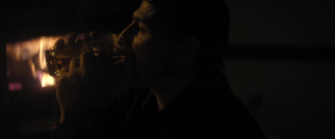 Close up of a man drinking and smoking in front of a fire