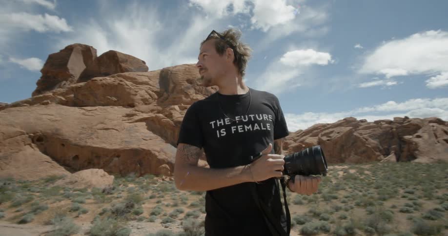 Man walking through the wilderness looking around while carrying his camera with large lenses attached