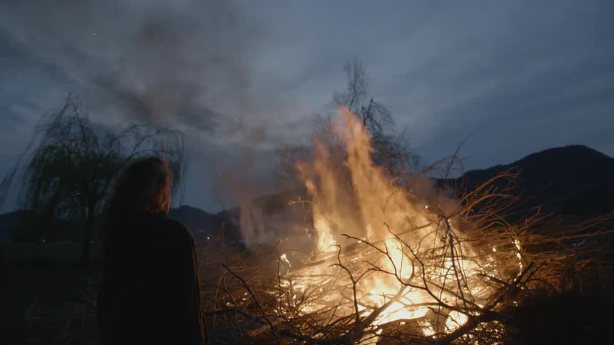 Girl standing next to a large bonfire at night
