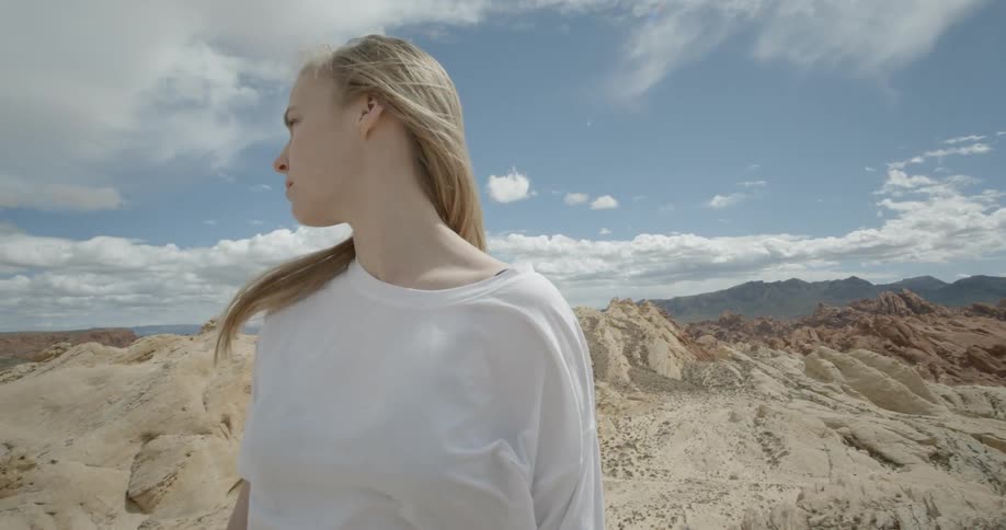 A woman is standing in a desert landscape during the day and looking around