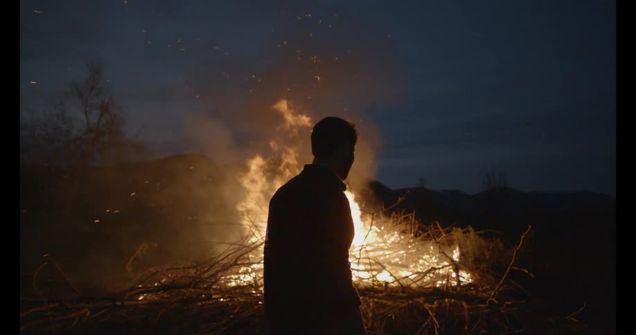 Man walking past a burning bonfire at night
