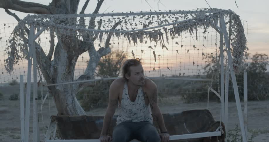 Man sitting on an outdoor bench at sunset  with wilderness behind him