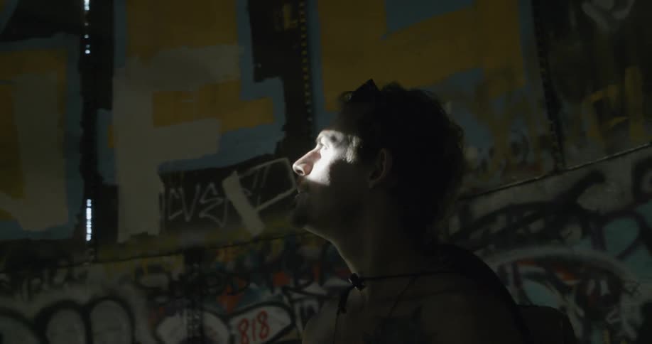 A man stands inside a building filled with graffiti staring up at the sun