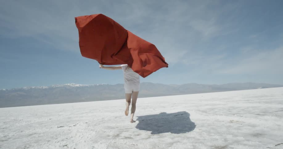 A woman walks over a field with a red cape behind her