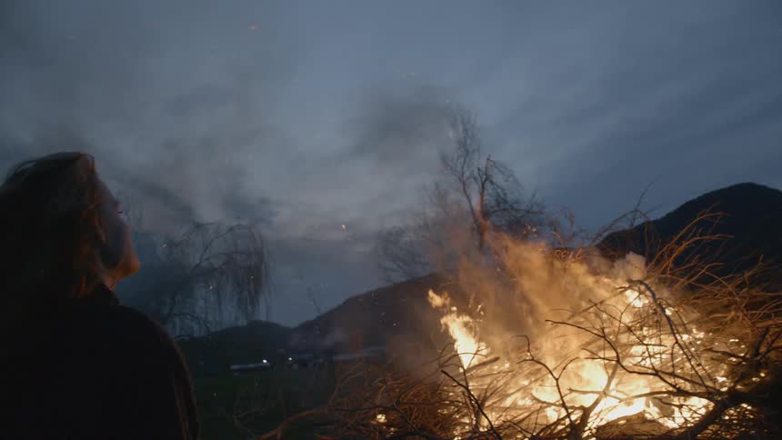 Girl standing next to bonfire at dusk