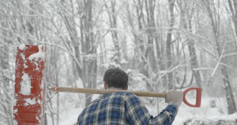 A man walking in the snow with a snow shovel over his shoulder