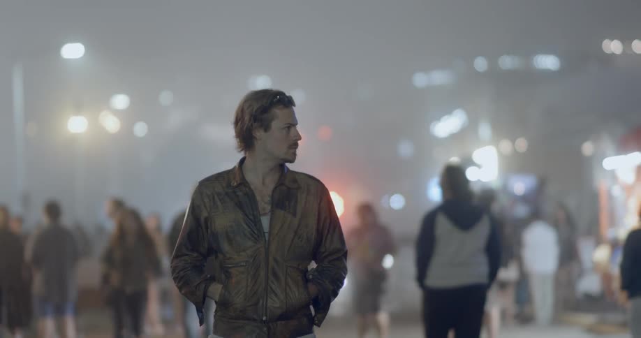 A man stands looking around in an area with a lot of people at night