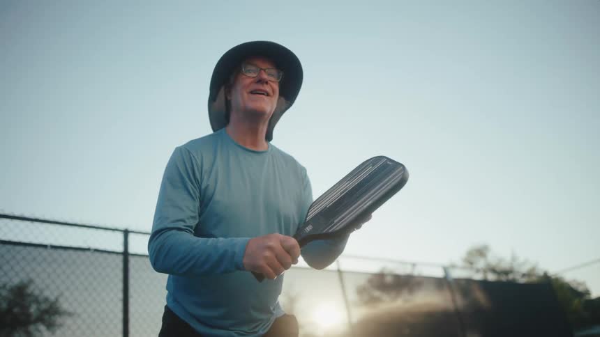 Elderly man holding a pickleball paddle preparing to return serve