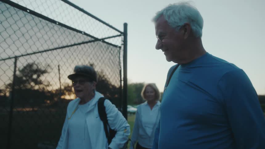 Four elderly people walking next to a tennis court while smiling and talking
