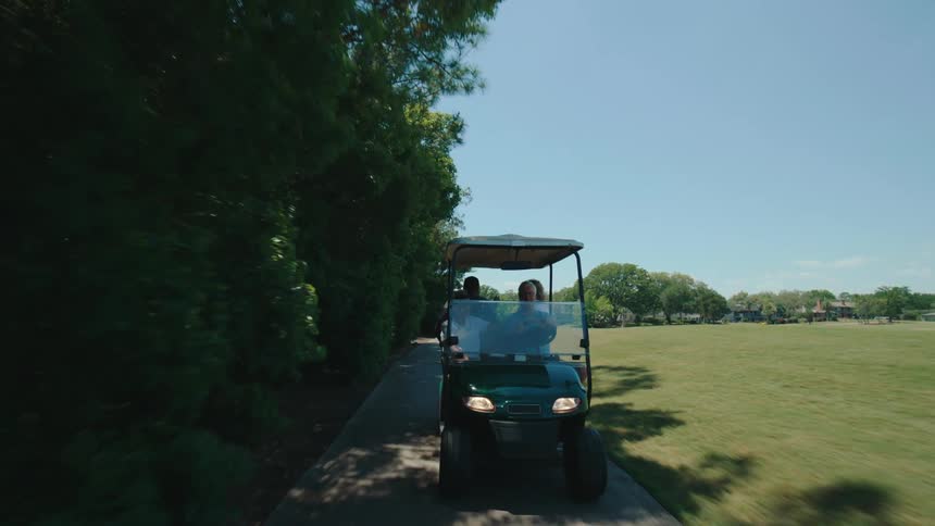 A golf cart driving on a path between grass fields on a clear day