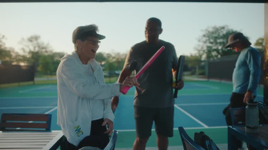 Friends discuss pickleball paddles while standing near tennis court