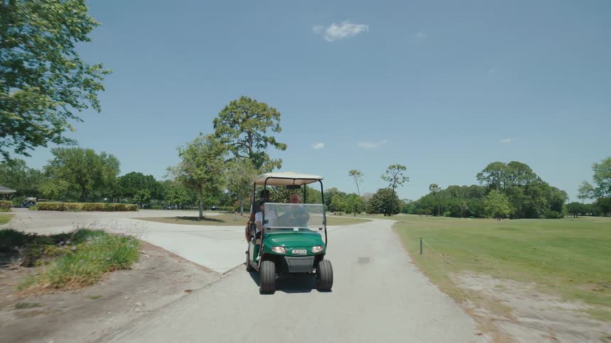 A green golf cart driving on a concrete path between green fields