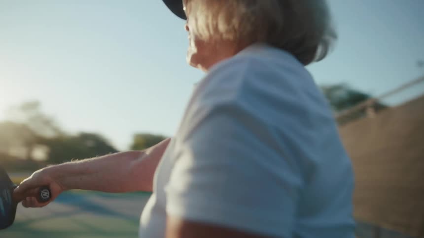 An elderly woman serves a pickleball on a pickleball court