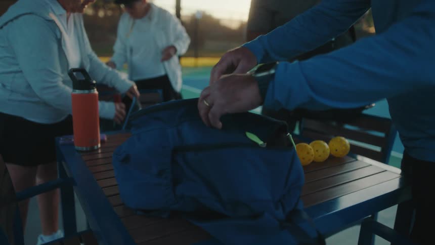 Four pickleball players unpack equipment and a thermos and water bottle from backpacks