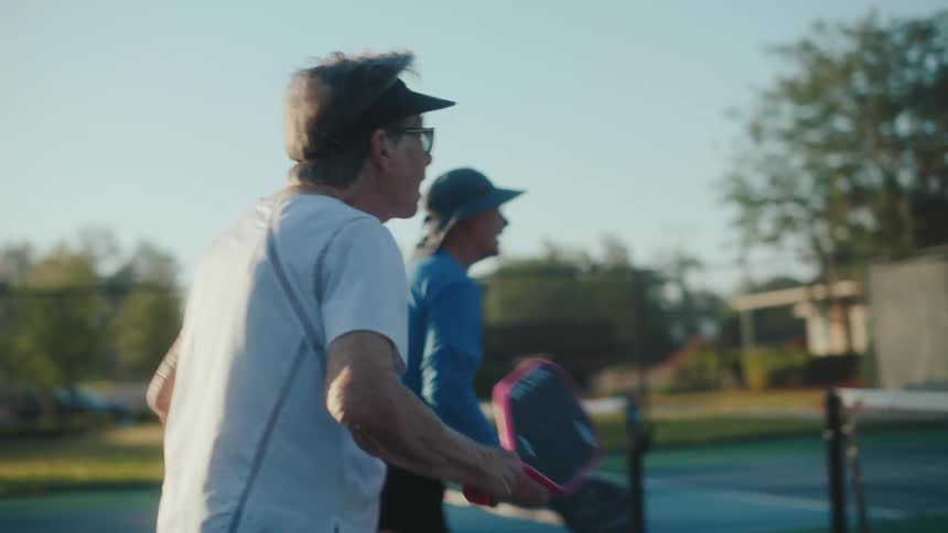 Two elderly people on a court playing pickleball