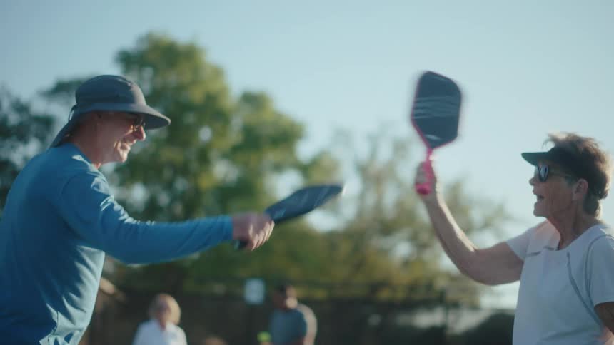 Elderly couple tapping paddles while playing pickleball