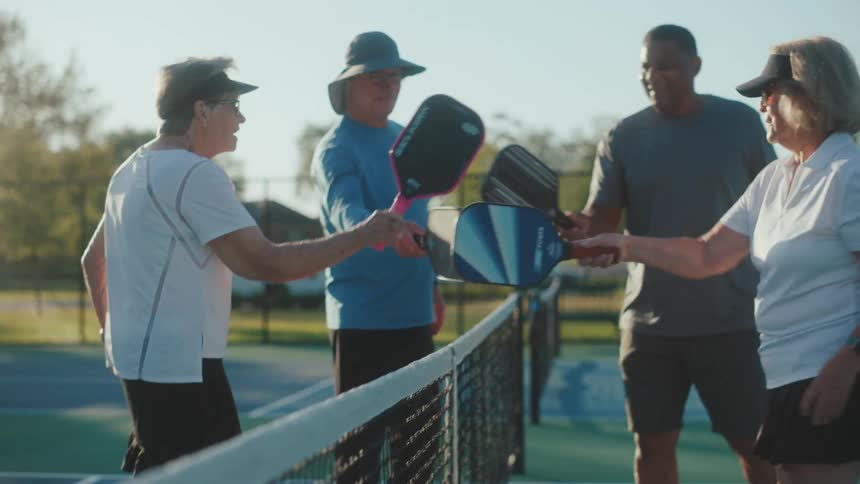 Four people walk to a pickleball net and tap paddles together