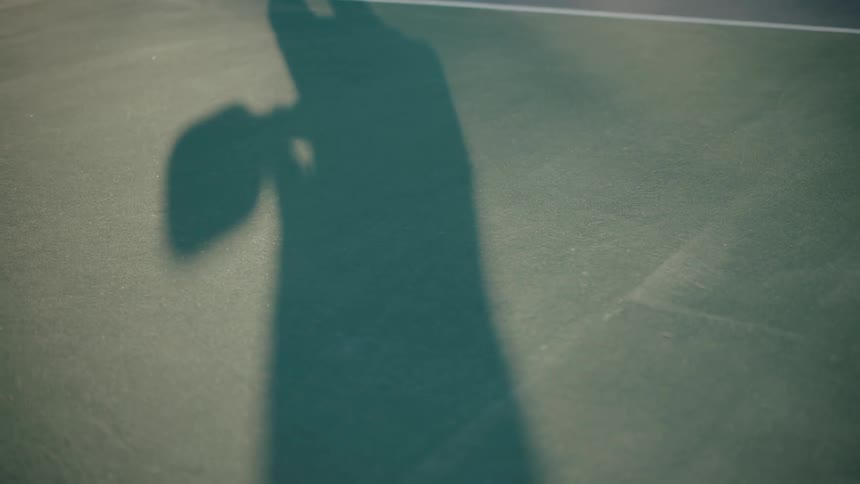 Shadow of a person playing pickleball on a court