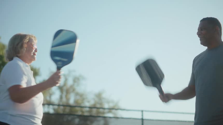 Man and woman high five with their pickleball paddles