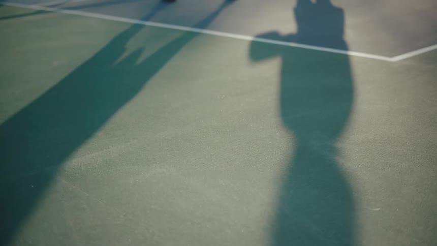 Shadow of two people with pickleball paddles moving across a tennis court