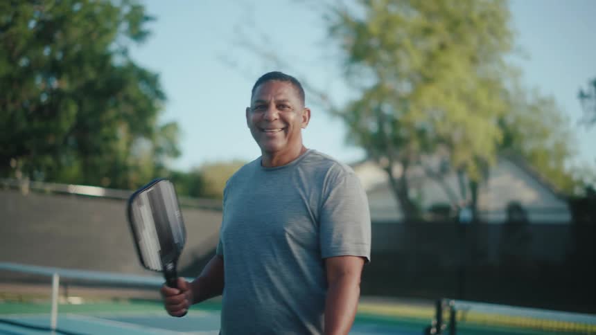 An ethnic man with a paddle and pickleball on a tennis court