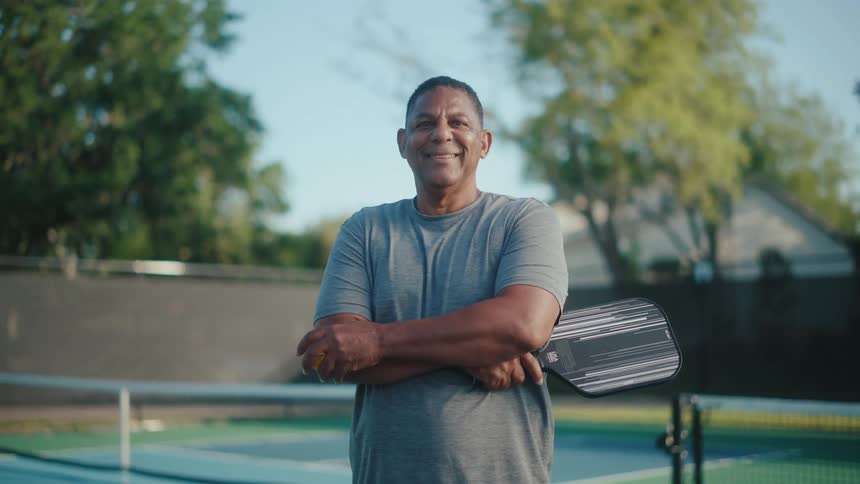 A man smiling while standing and holding a pickleball paddle
