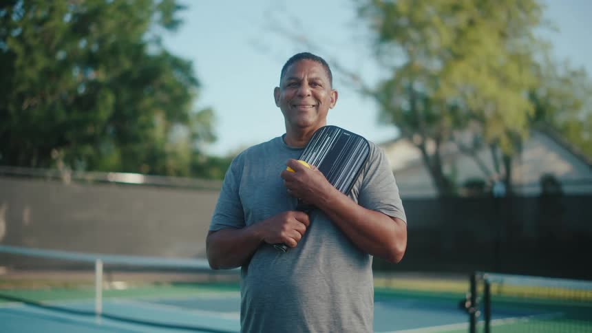 Smiling man with a racket in his hand next to a tennis court