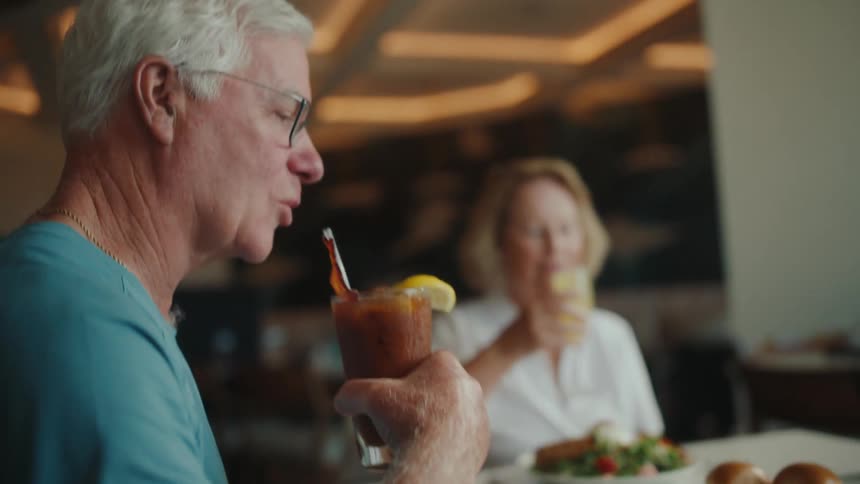 An elderly man takes a sip of a bloody mary drink