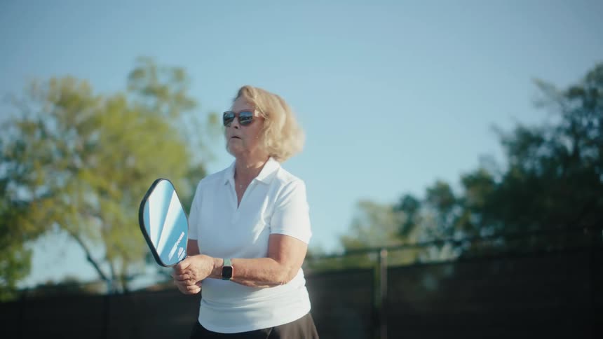 Elderly lady with sunglasses on a court playing pickleball