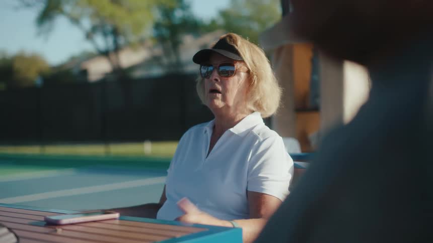 Woman with sunglasses sitting at a table next to a tennis court