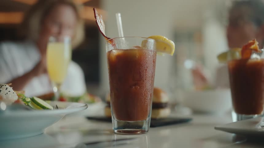 A bloody mary drink sits on a table where two elderly women are eating and talking