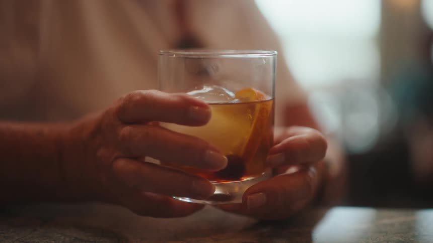 Glass cup with a drink and a womans hands holding it