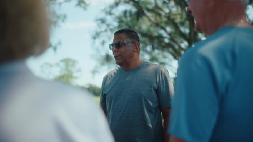 Older adult friends stand outdoors during the day talking together