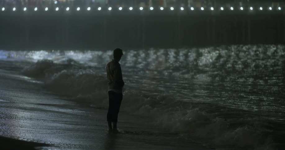 Person standing on a beach at night with lights in the distance