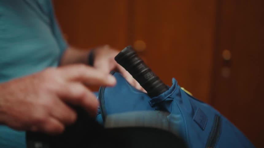 A man puts his pickleball paddle inside of his backpack and leaves the locker room