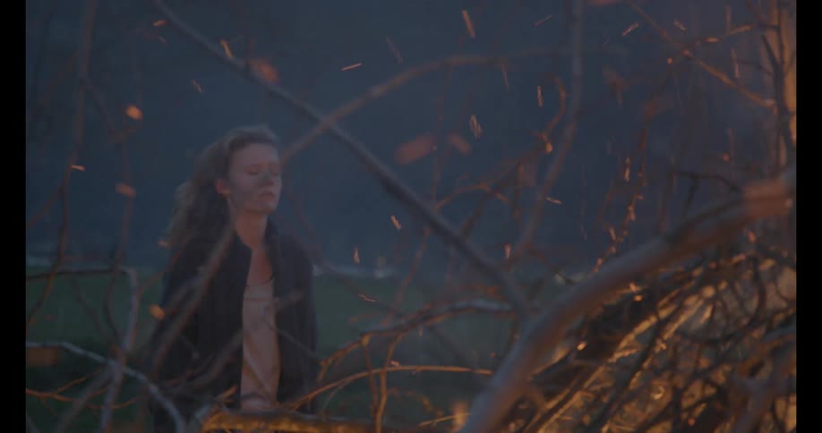 A woman watches a bonfire as embers rise