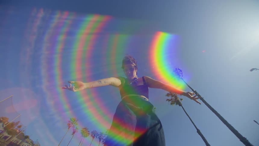 A woman is standing making gestures with her arms and there is a flare of colored lights in front of her