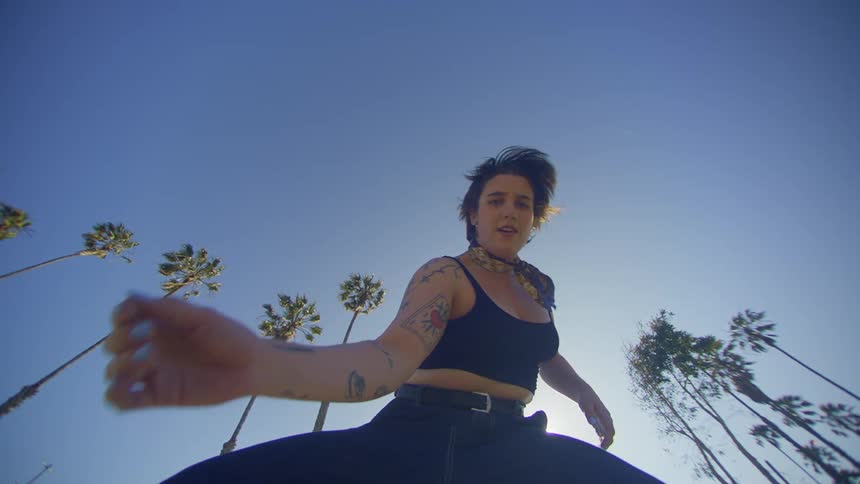 Sun glares down on woman dancing outdoors near palm trees