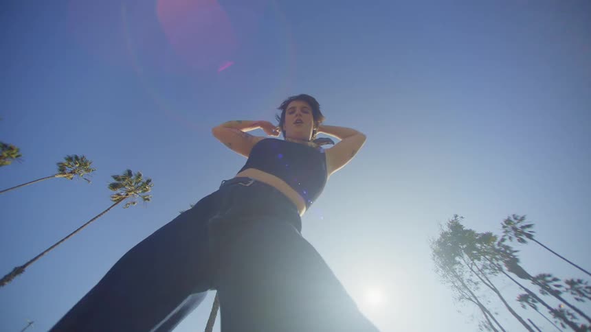 A woman dances against a clear blue sky surrounded by tall slender palm trees