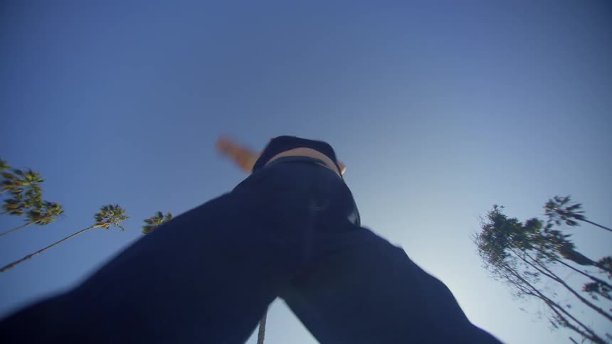 A woman dances against a clear blue sky surrounded by tall slender palm trees