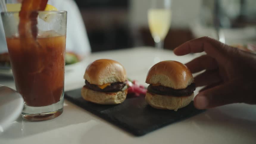 A black man grabs a small burger from a tray on a table in a restaurant