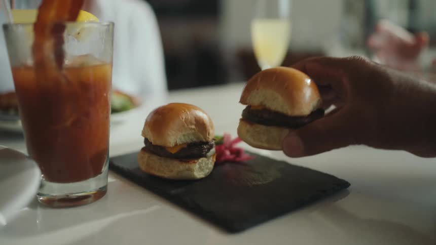 Persons hand picking up a small hamburger on the table