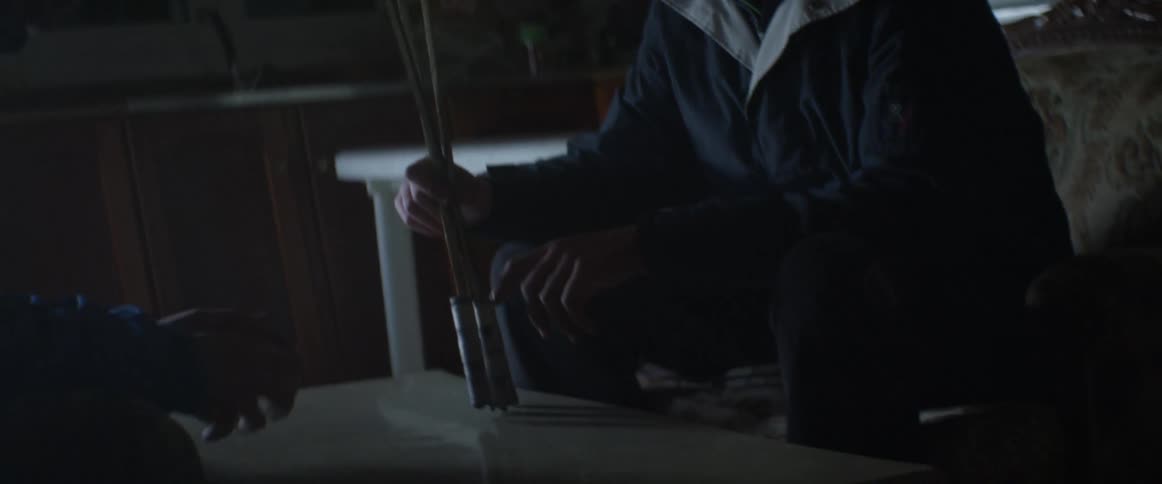 Two men sit and talk in a living room as one of them holds and plays with arrow bolts