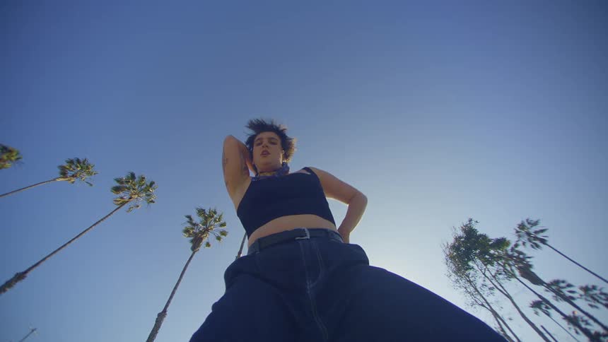 A woman with tattoos dances outdoors at midday