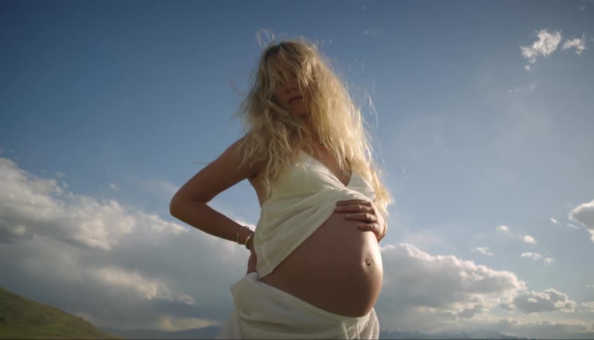 A pregnant blonde woman standing in a field