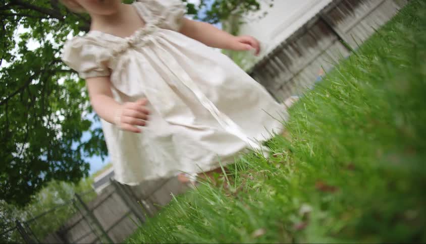 A toddler reaches for grass as her mother and siblings sit in the background