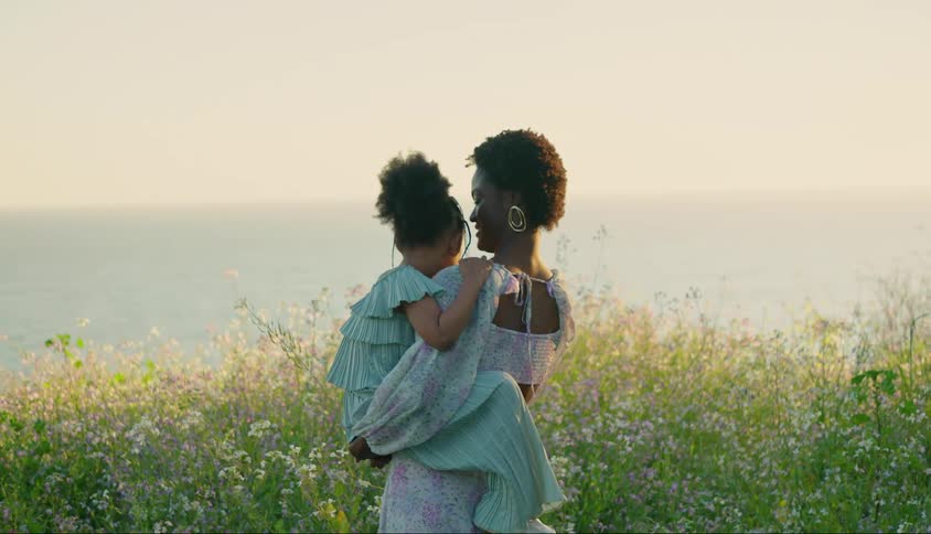Mother holding her daughter on her lap while they are in a natural setting in a flower garden by the sea