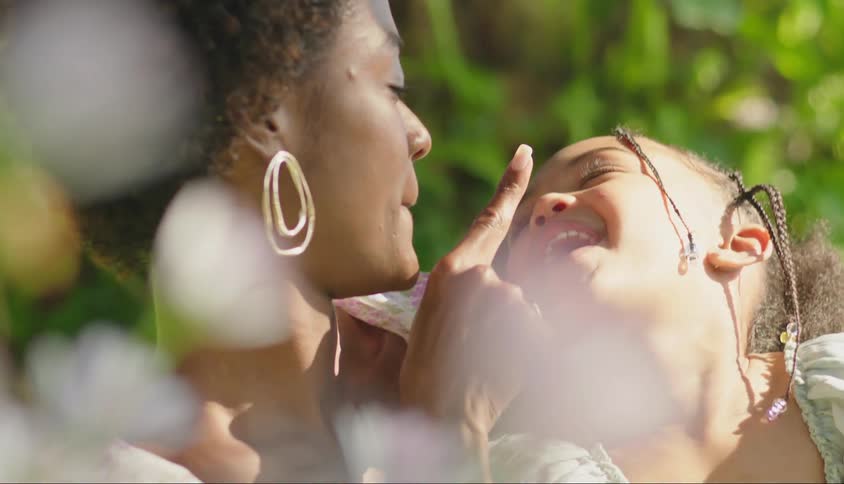 A mother holds her daughter outdoors while they touch each others faces