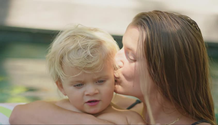 Portrait of the mother in the pool giving a kiss to her son who is on the float